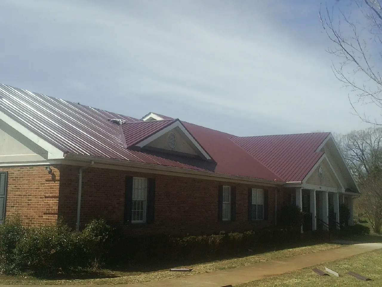 Red metal roof with gabled entries on a long brick building, from a Hail Damage Roof Repair job in Chesterfield